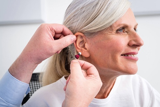 Ältere Frau lächelt beim Anpassen eines modernen Hörgeräts durch einen Hörakustiker.